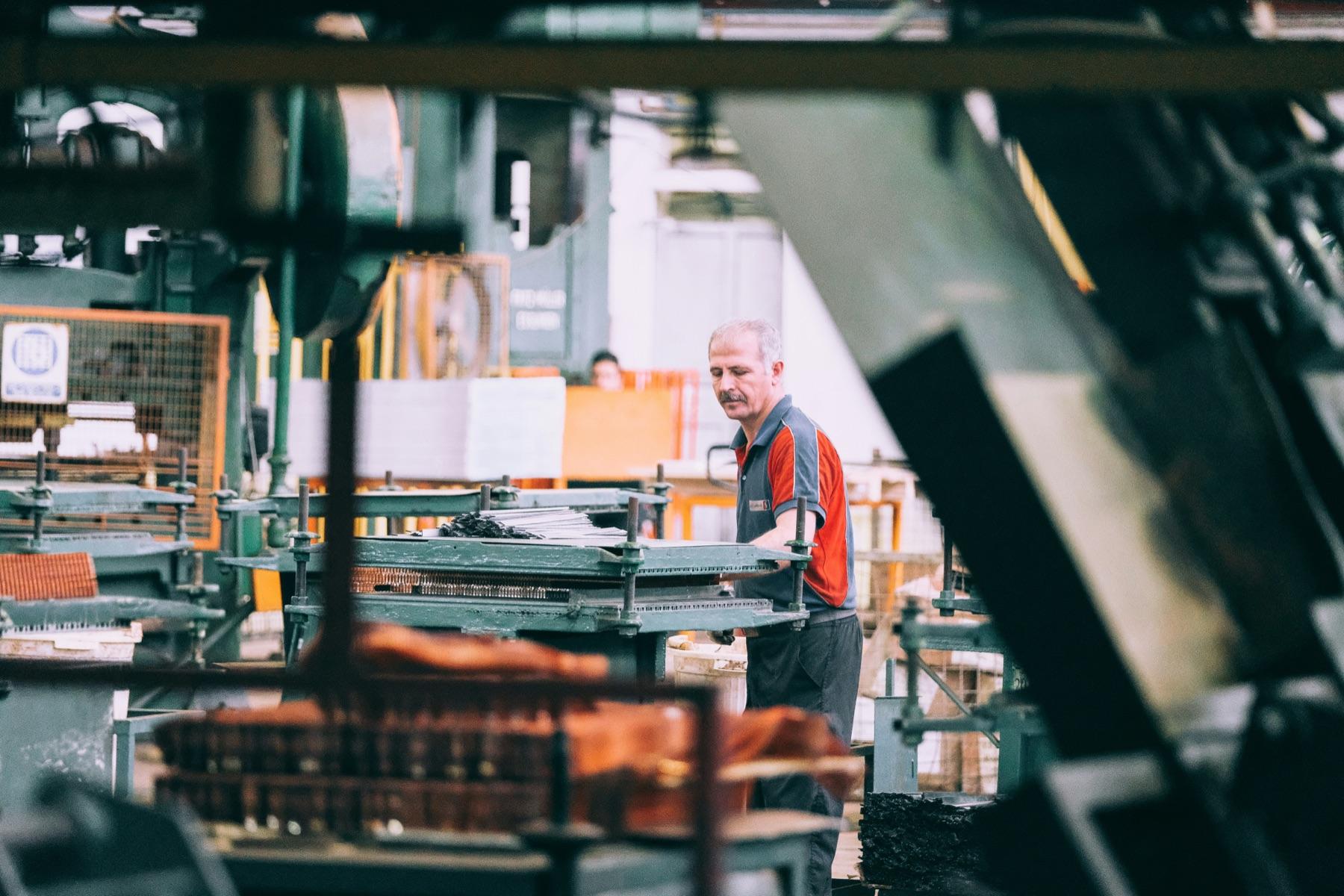 Employé d'usine qui manipule des pièces métalliques à un poste de presse, entouré de machinerie
