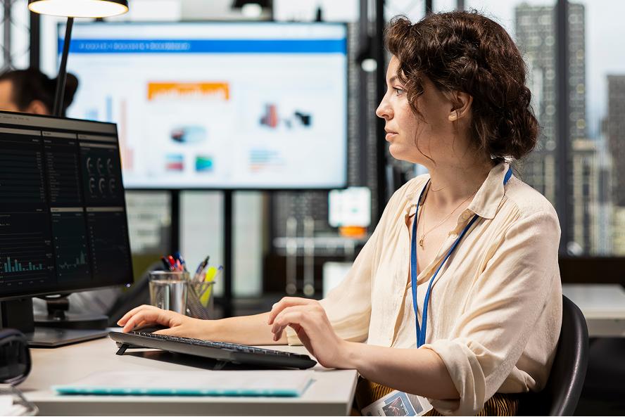 Employée travaillant à un poste informatique devant des écrans de production